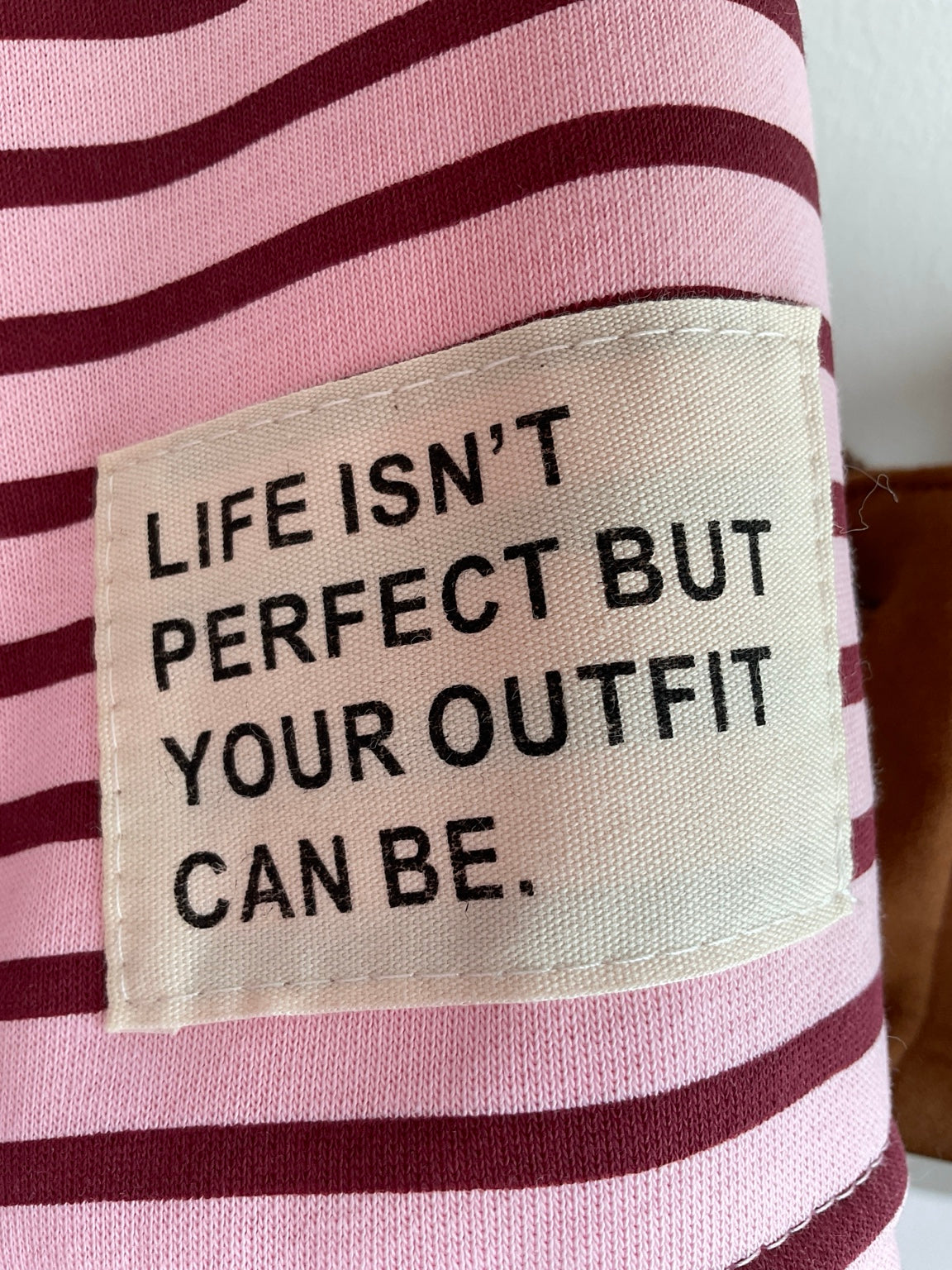 Detalle de etiqueta decorativa en sudadera de rayas rosa y burdeos